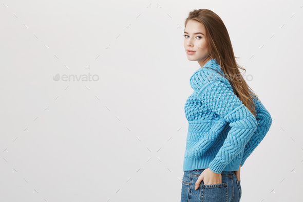 Indoor shot of attractive seductive woman turning back to camera while holding hands in back pockets