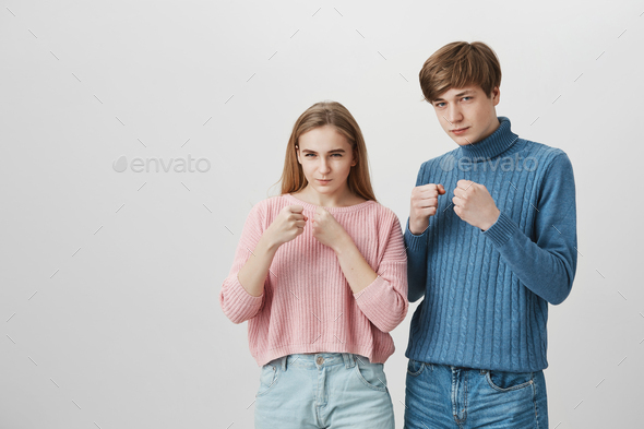 Blonde girl and fair-haired guy standing indoors with fists bunched and determined face expressions