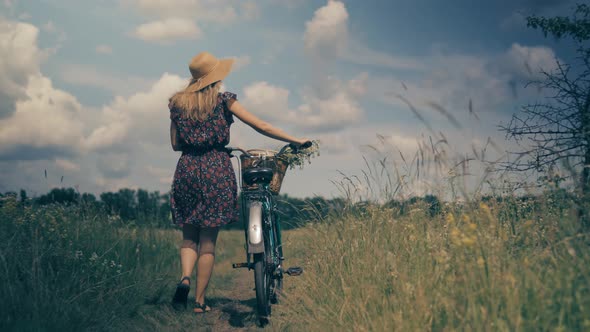 Woman In Hat Enjoying Weekend.Woman Cyclist Walking With Bike On Holiday Vacation Trip. Wildflower. alt