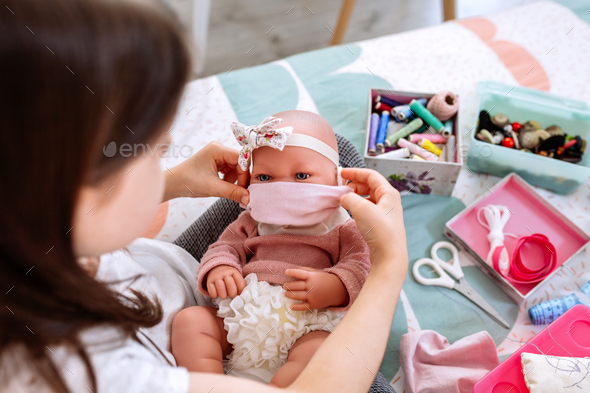 Girl trying on her doll a mask that she is sewing