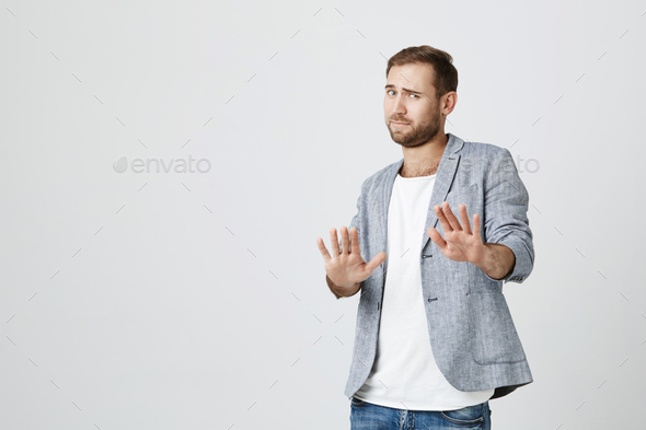 Attractive bearded man makes frightened gesture with palms, defends himself from someone, asks to