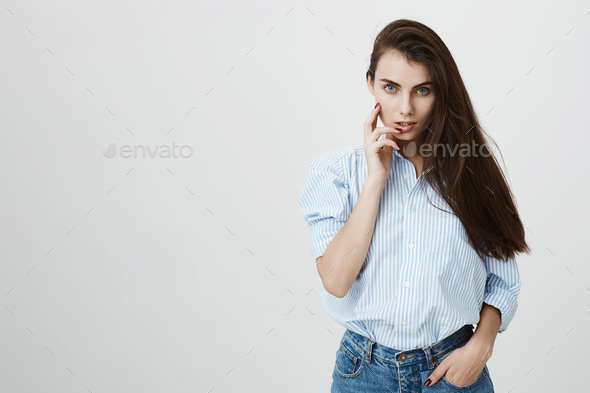 Hot and sensual european woman in blue-collar shirt flirting and glancing at camera with hand near