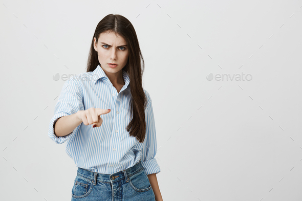 Studio portrait of young european woman in blue-collar shirt, expressing aggression with eyes and