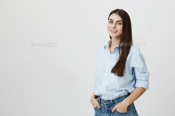 Confident and attractive business woman standing in blue-collar shirt with hands in pockets over