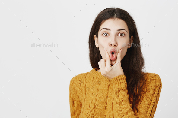 Portrait of funny attractive european female squeezing opened mouth and staring at camera with