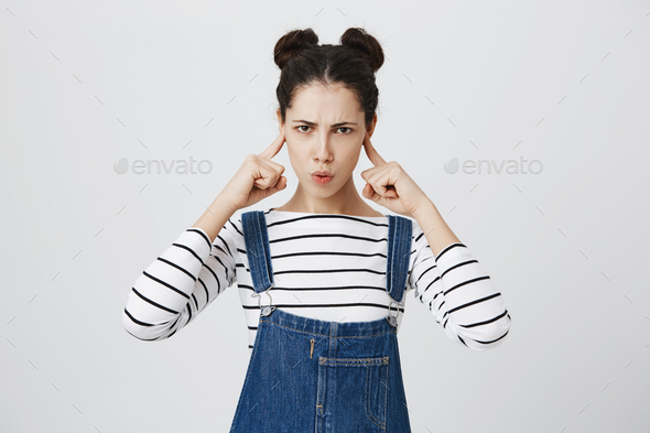 Stressed funny brunette girl plugs ears, avoids loud sounds at street, doesn`t want to listen noise