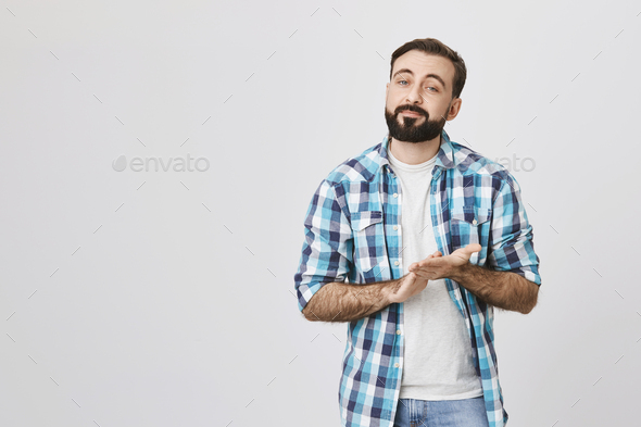 Portrait of pleased caucasian guy with stylish haircut rubbing hands, wearing checked shirt and