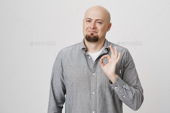 Portrait of attractive smiling bald man with beard showing okay sign and standing with not bad