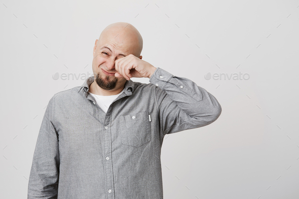 Portrait of attractive sleepy guy with beard rubbing his eye over white background. Man feels tired
