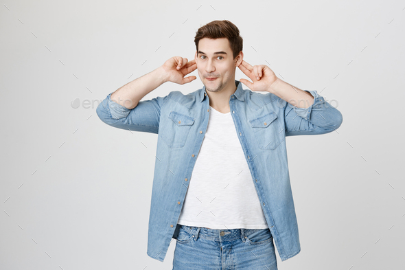Stressed funny dark-haired man plugs ears, avoids loud sounds at street, doesn`t want to hear noise