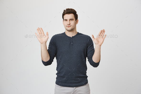 Scared young man makes frightened gesture with palms, defends himself from someone, asks to stop it