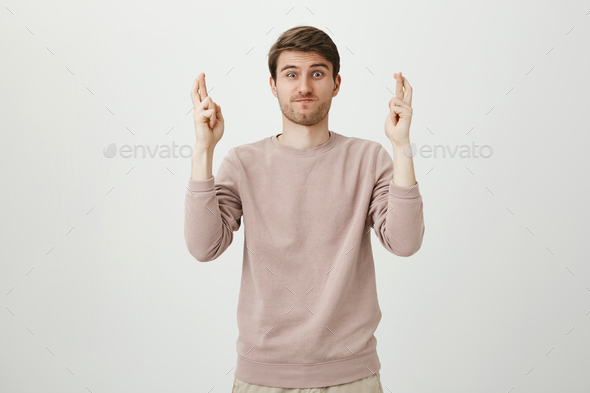 Portrait of funny attractive caucasian man raising hands with crossed fingers, holding breath and