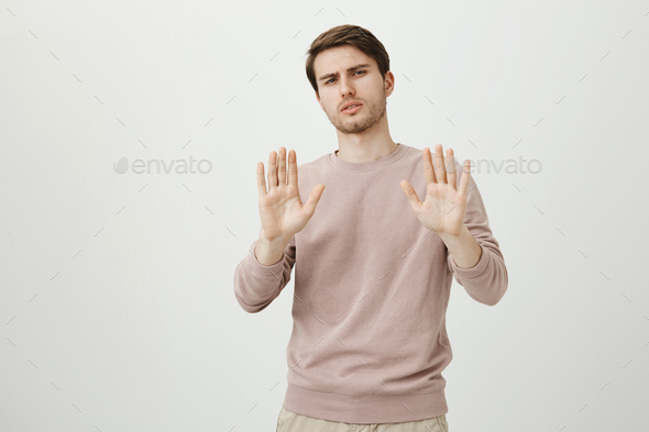 Serious and confident good-looking guy holding hands in stop or enough gesture, bending behind and