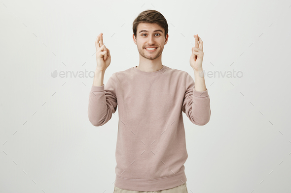 Portrait of charming caucasian male with bristle raising hands with crossed fingers and smiling