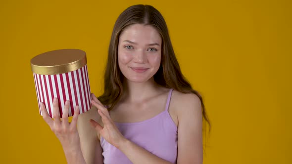 Young happy girl in dress posing with gift box isolated on yellow background.