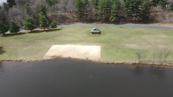 Aerial view of lake and park in midwest in fall with a small beach and shelter area on the edge.