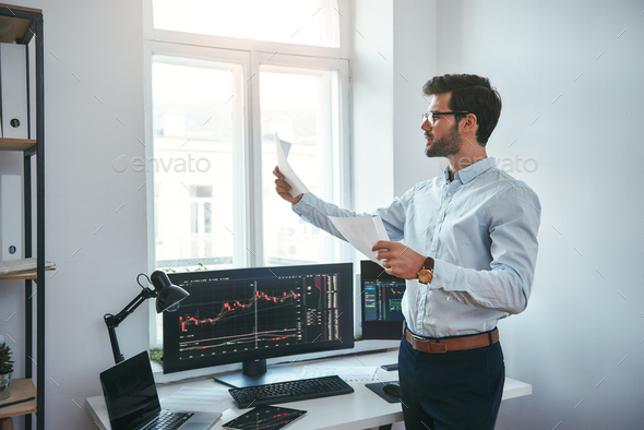 Trading strategy. Smart and young trader in eyeglasses looking at financial reports and analyzing - Stock Photo - Images