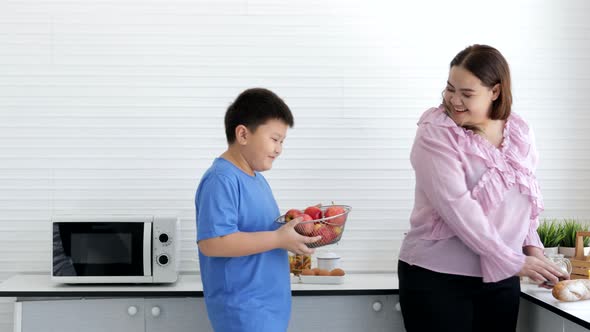 Overweight young mother and son standing and eating apple deliciously in the kitchen