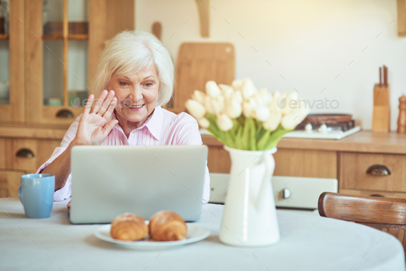 Smiling senior woman waving at screen while chatting during video call