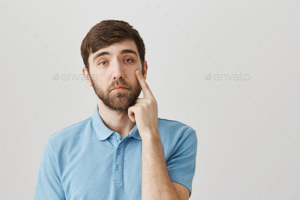 You have not impressed me. Studio shot of ordinary young bearded guy holding index finger on face