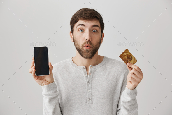 Have you heard about online shopping. Handsome curious man showing smartphone and credit card