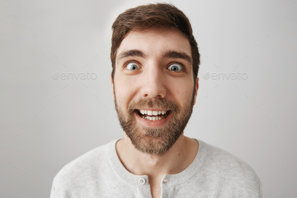 Close-up portrait of funny bearded guy making faces at camera, smiling and acting like crazy