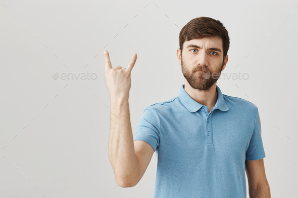 Rock n roll is alive. Portrait of serious cool european bearded man showing rock gesture with raised