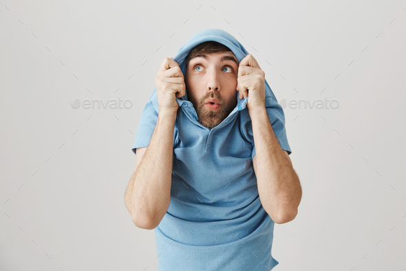 Positive funny european male pulling shirt on head and staring through collar up as if seeing some