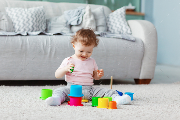 The kid plays on the floor on a light carpet with bright toys, builds a tower