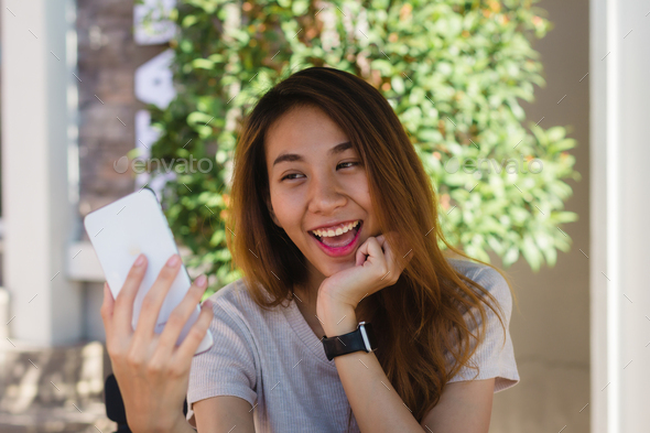 Attractive beautiful happy young Asian woman taking a selfie using a smart phone at cafe. - Stock Photo - Images