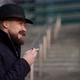 a Mustachioed and Bearded Stylish Man in a Hat and a Dark Coat Smokes a Cigarette on the Stairs Out - VideoHive Item for Sale