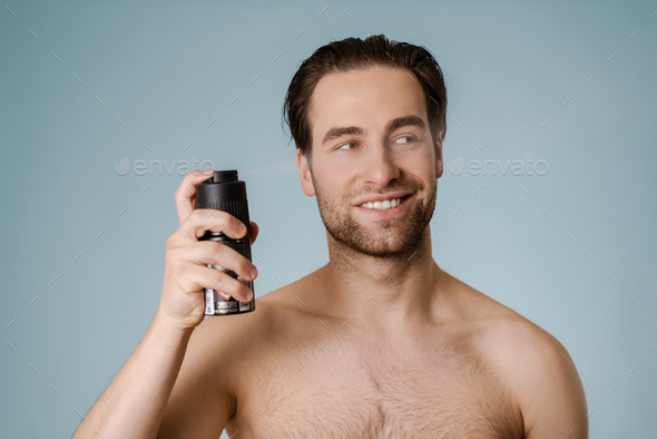 Handsome smiling nude man spraying deodorant Stock Photo by vadymvdrobot
