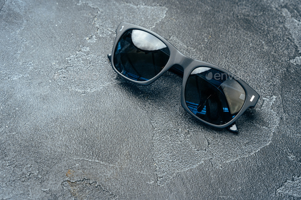 Dark male sunglasses on grey concrete surface Stock Photo by FabrikaPhoto