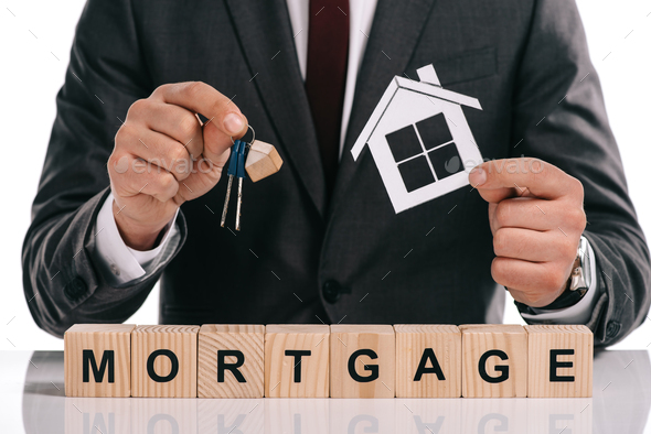 cropped view of mortgage broker holding paper house and keys near wooden blocks isolated on white