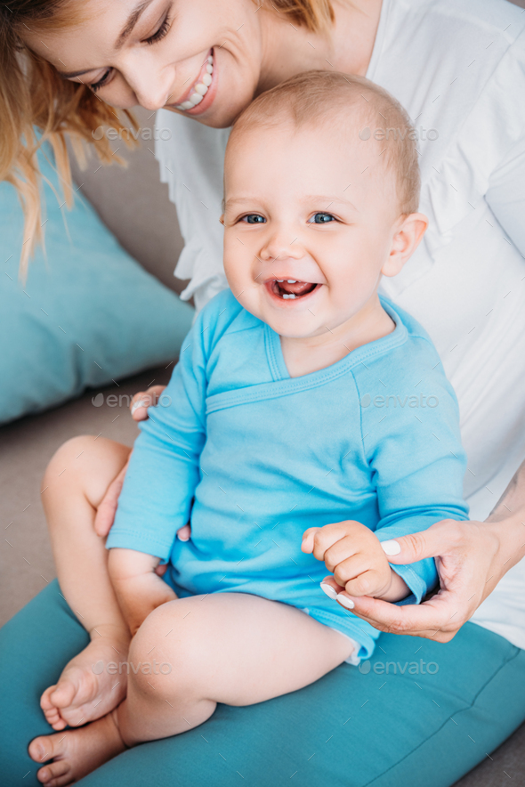 close-up portrait of laughing little child sitting on knees of mother ...