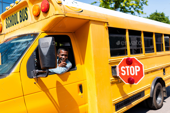 smiling mature african american bus driver looking out window and gesturing - Stock Photo - Images