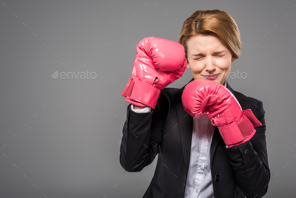 stressed businesswoman in suit and pink boxing gloves, isolated on grey
