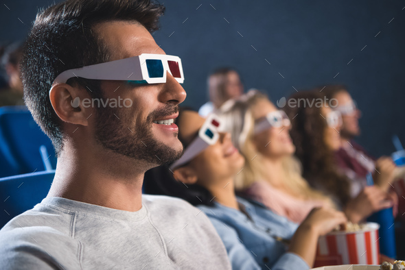 selective focus of multiethnic friends in 3d glasses with popcorn watching film together in movie