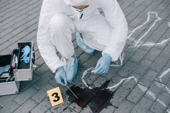 male criminologist in protective suit and latex gloves taking a blood ...