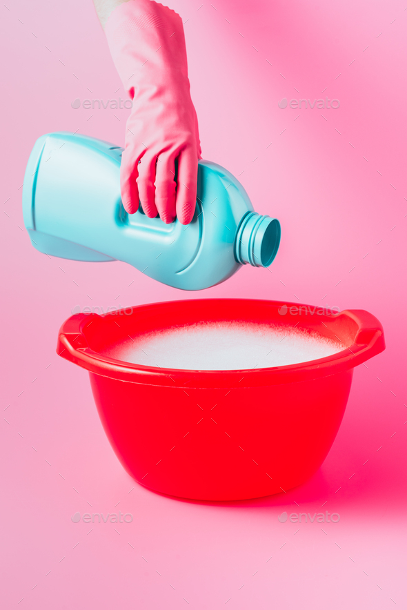 partial view of female cleaner pouring laundry liquid in plastic basin with foam, pink background