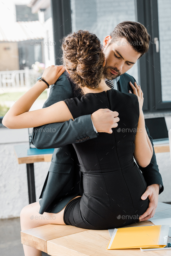 passionate businessman unzipping dress of seductive businesswoman at workplace in office Stock