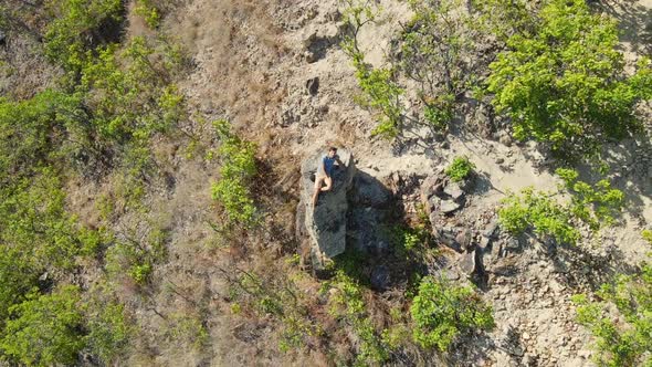 Aerial Shot of a Young Man Sitting on a Rock in Mountains. Hiking Concept alt