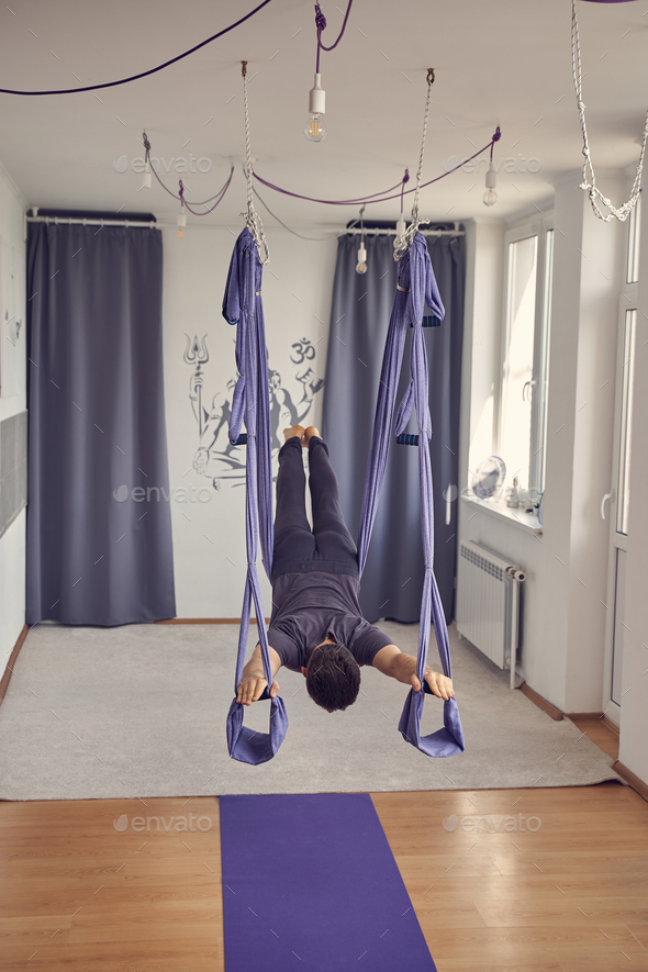 Athletic man using blue hammock swing for aerial yoga