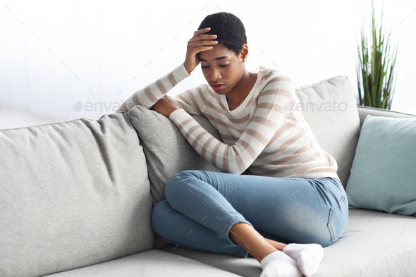 Seasonal Depression. Portrait Of Sad Black Female Sitting On Sofa At Home