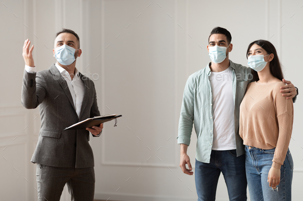 Estate Agent In Medical Mask Showing Buyers New Apartment