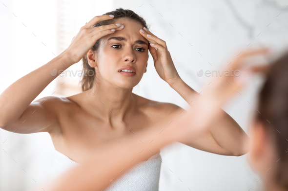 Frustrated Lady Squeezing Pimple On Forehead In Modern Bathroom Indoors
