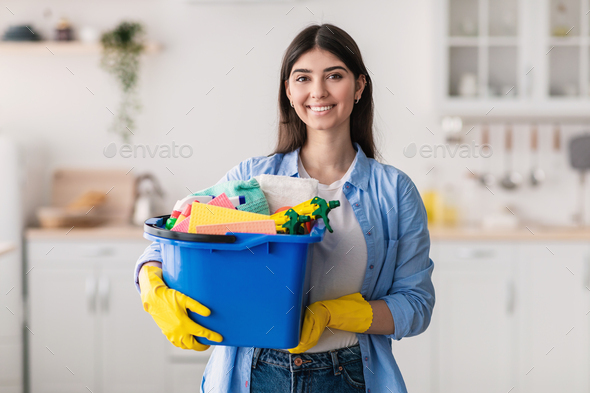 Cheerful Young Housewife Holding Bucket With Cleaning Supplies