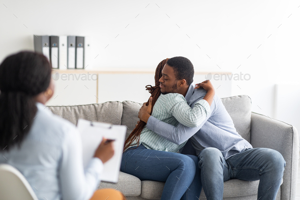 Happy black couple hugging in counselor's office after successful marital therapy