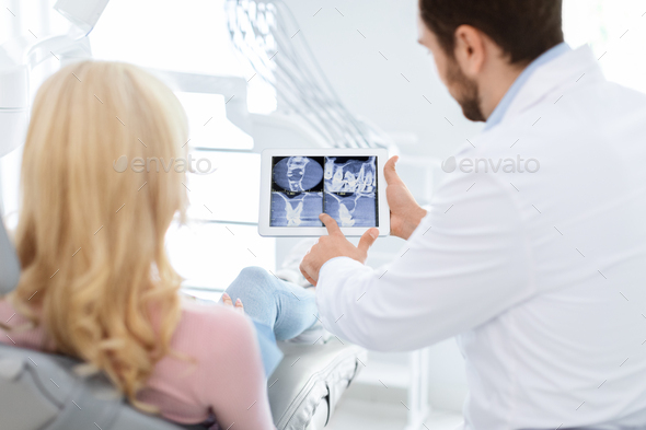 Man dentist showing female patient treatment goal, using tablet