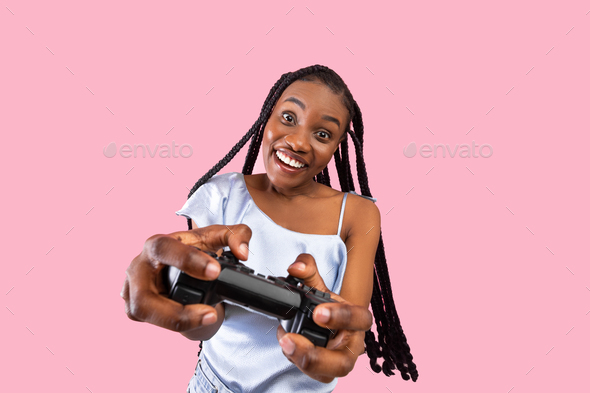 Millennial black lady with joystick playing exciting video game on pink studio background